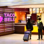FILE - In this April 19, 2019 file photo, travelers look at a menu at a Taco Bell restaurant inside Miami International Airport in Miami. The company that owns KFC and Taco Bell posted better-than-expected sales in the second quarter thanks to stronger customer demand and a record new store building spree. (AP Photo/Wilfredo Lee, File)